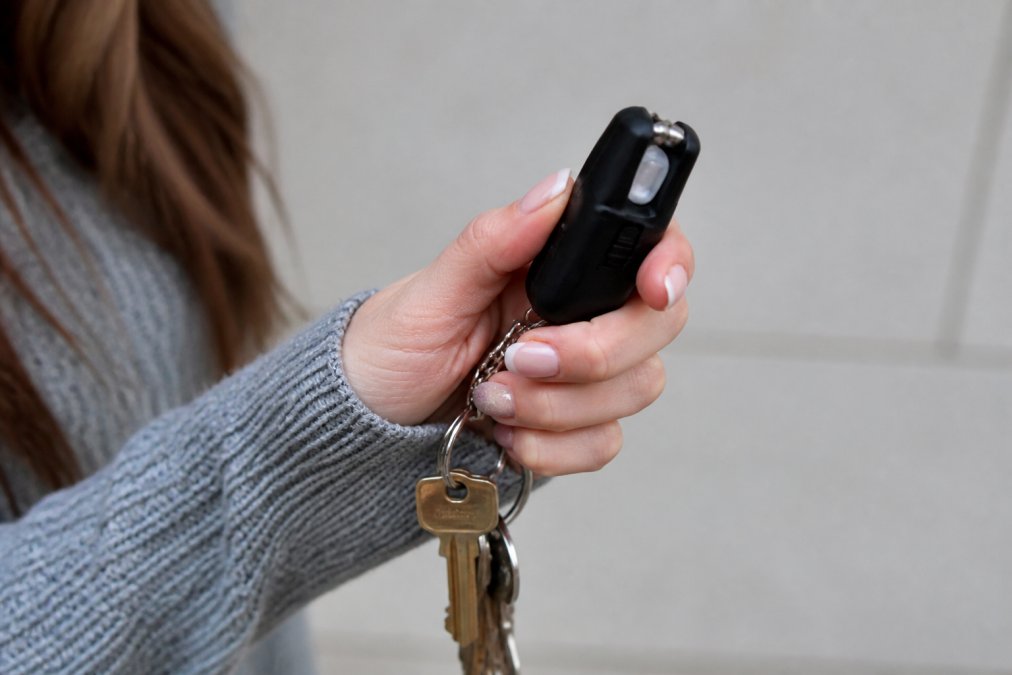 Close-up of a woman's hand holding a compact keychain stun gun with LED flashlight displayed against a neutral background with keys attached