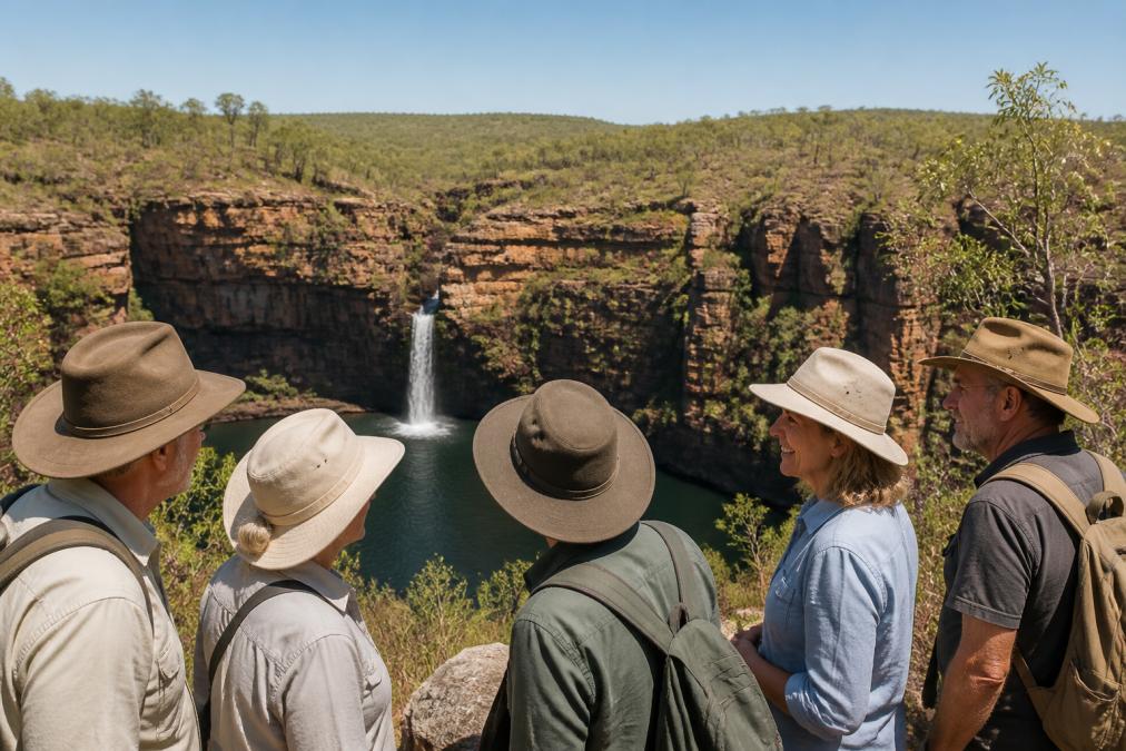Small group of mature travellers standing together at a scenic gorge overlook with red-rock cliffs and a waterfall cascading into a pool below, all wearing wide-brimmed hats and smiling while looking out at the wilderness landscape