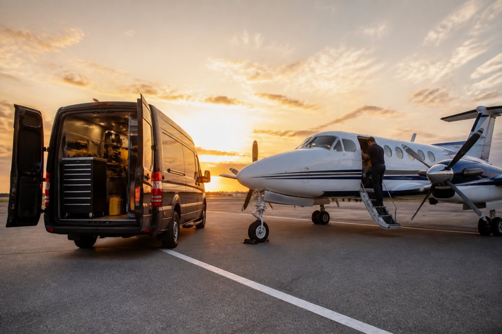 Mobile maintenance van parked beside King Air aircraft on tarmac at dawn with technician accessing aircraft door