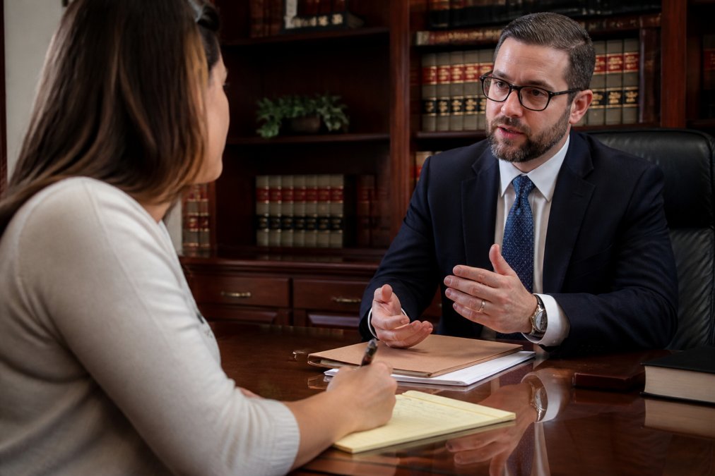 Client taking detailed notes during consultation with attorney, asking questions about case strategy and legal timeline with professional office setting