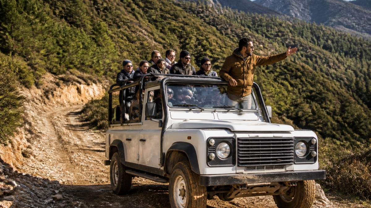 Deneyimli rehber tarafından yönetilen jeep safari aracında turist grubu, arka planda Fethiye'nin dağlık ve yeşil arazisi, güneşli kış günü