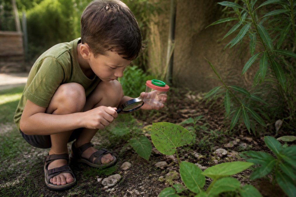 Enfant observant une feuille dans le jardin avec les outils de son kit d'observation nature et une loupe.