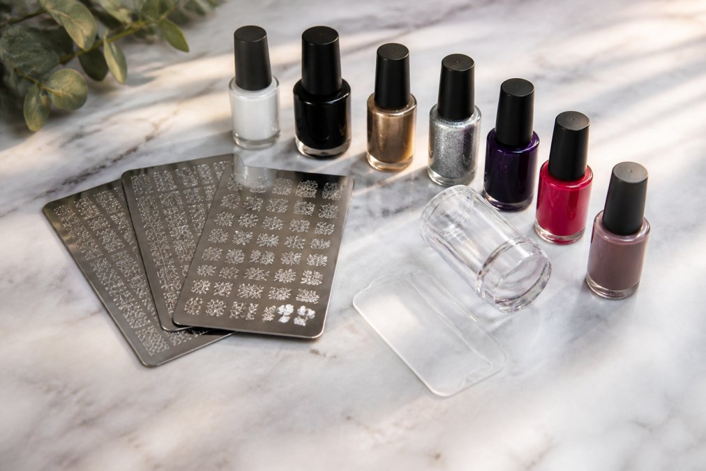 Flat lay d'un kit complet de stamping ongles sur une surface en marbre blanc : plaques de stamping en acier inoxydable, tampon en silicone transparent, raclette, petits flacons de vernis à stamping en plusieurs couleurs, disposés soigneusement sous un éclairage naturel
