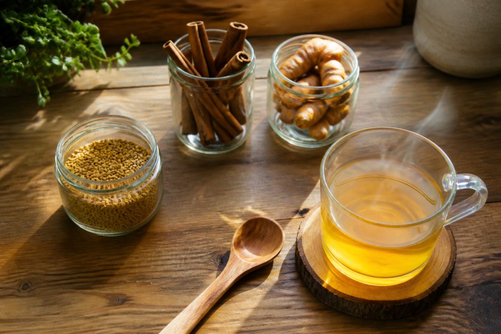 Cinnamon, turmeric, and fenugreek on a counter next to herbal tea to support insulin sensitivity