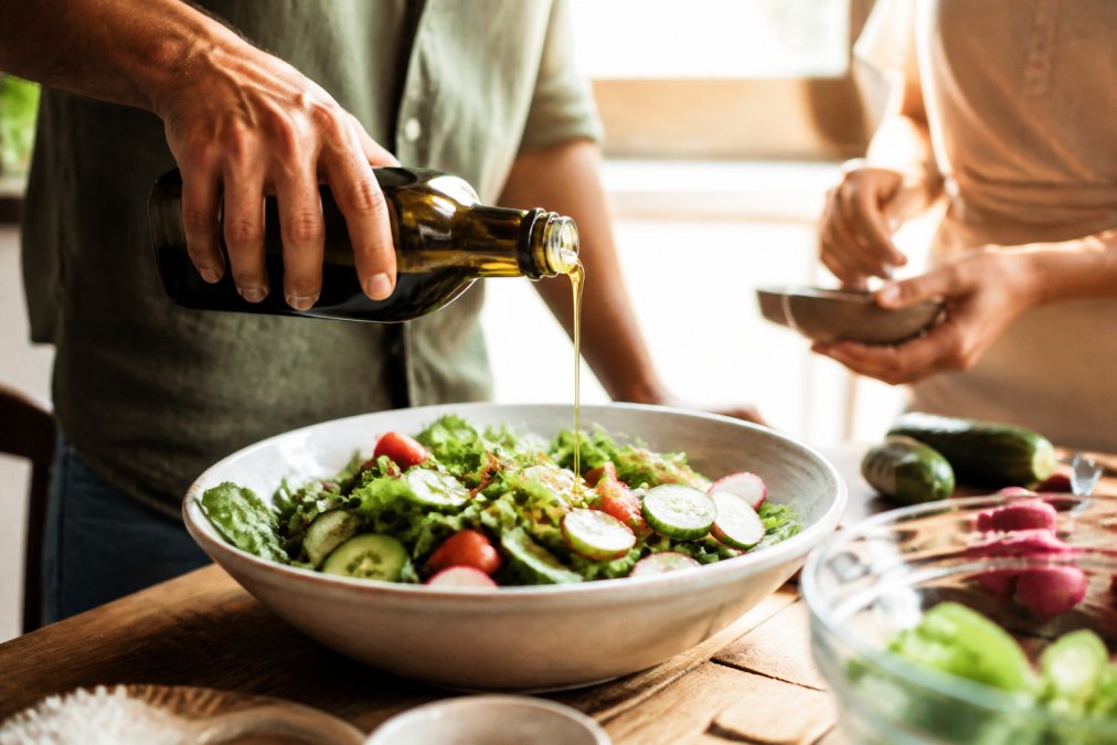 Verfijnde groene salade met vers gesneden groenten, afgewerkt met een gouden druppel extra virgin olijfolie en een snufje zout, natuurlijk daglicht dat de olie doet glanzen