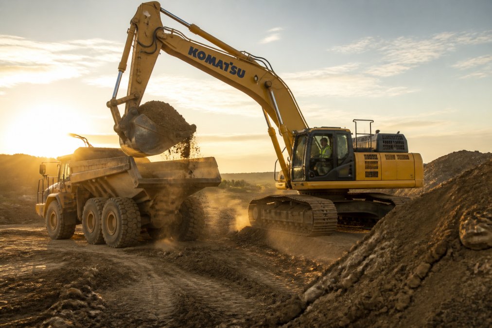 Large Komatsu equipment excavator loading dirt into a dump truck at sunset