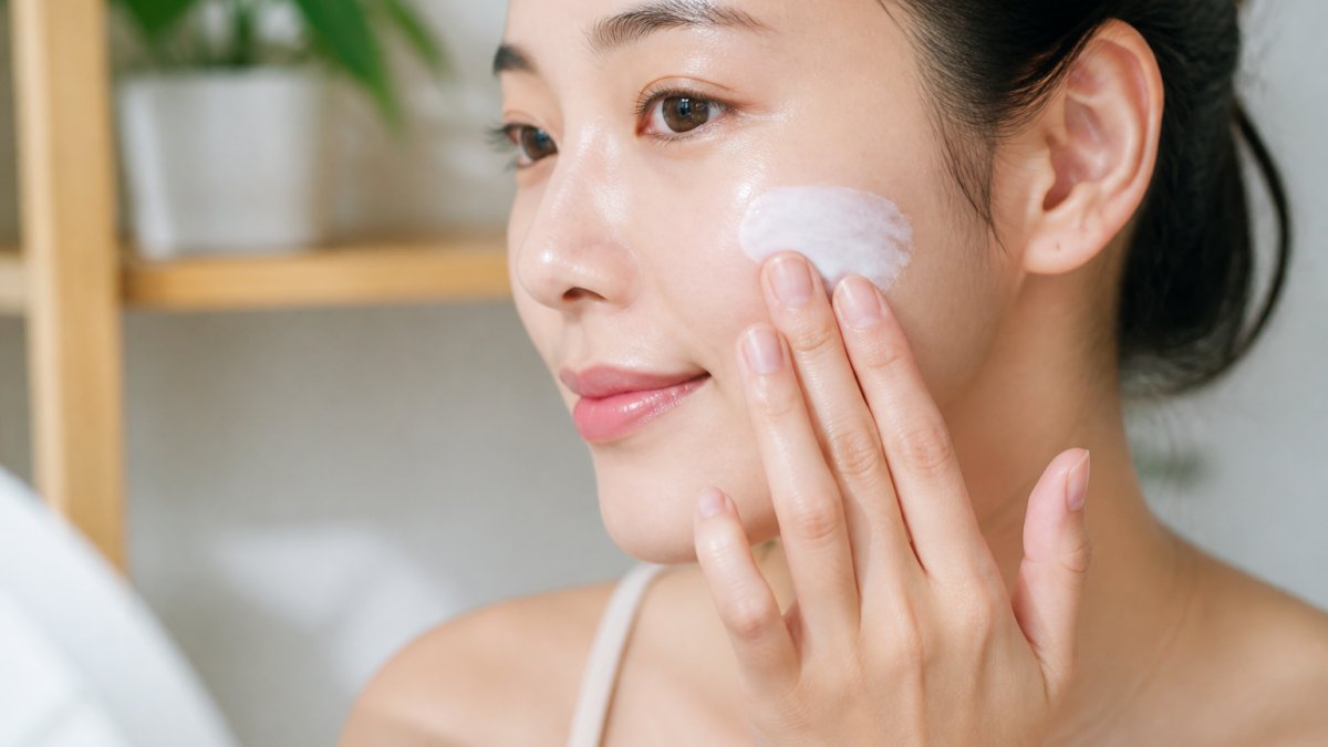 Close-up of hands applying lightweight Korean sunscreen over moisturized skin, showing proper layering technique with visible dewy product texture and smooth absorption on complexion