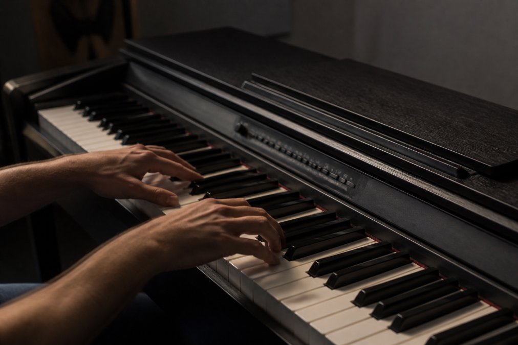 Musician's hands positioned on Korg digital piano keyboard showing weighted key action, with proper finger posture and natural studio lighting highlighting the keyboard mechanics