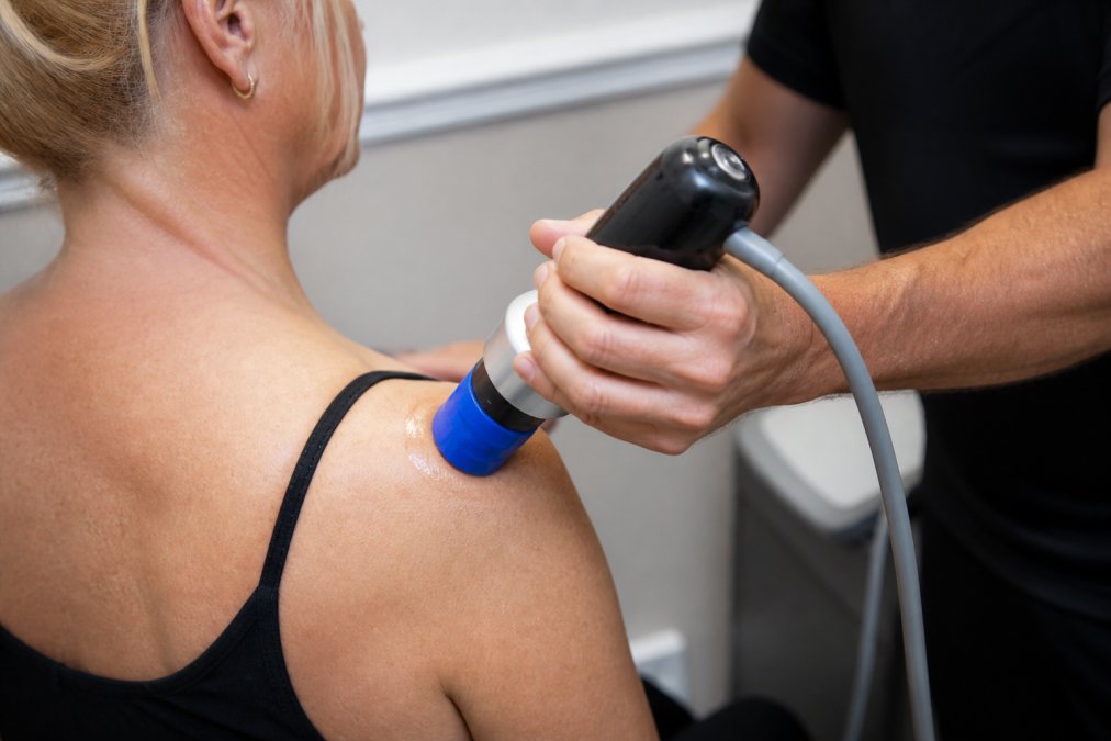 Close-up of PiezoWave 2 acoustic wave therapy device being applied to patient's shoulder during treatment session in clinical setting