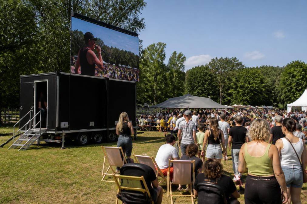 Een professionele LED-aanhangwagen van LED-AD opgesteld op een druk buitenevenement in België, met een helder verlicht 10m² LED scherm zichtbaar in daglicht, omringd door publiek en uitgestrekte festivalterreinen