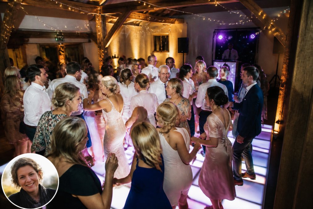 Een verlichte dansvloer op een bruiloftsfeest met gasten die dansen, warme sfeerverlichting en een DJ op de achtergrond in een sfeervolle feestlocatie