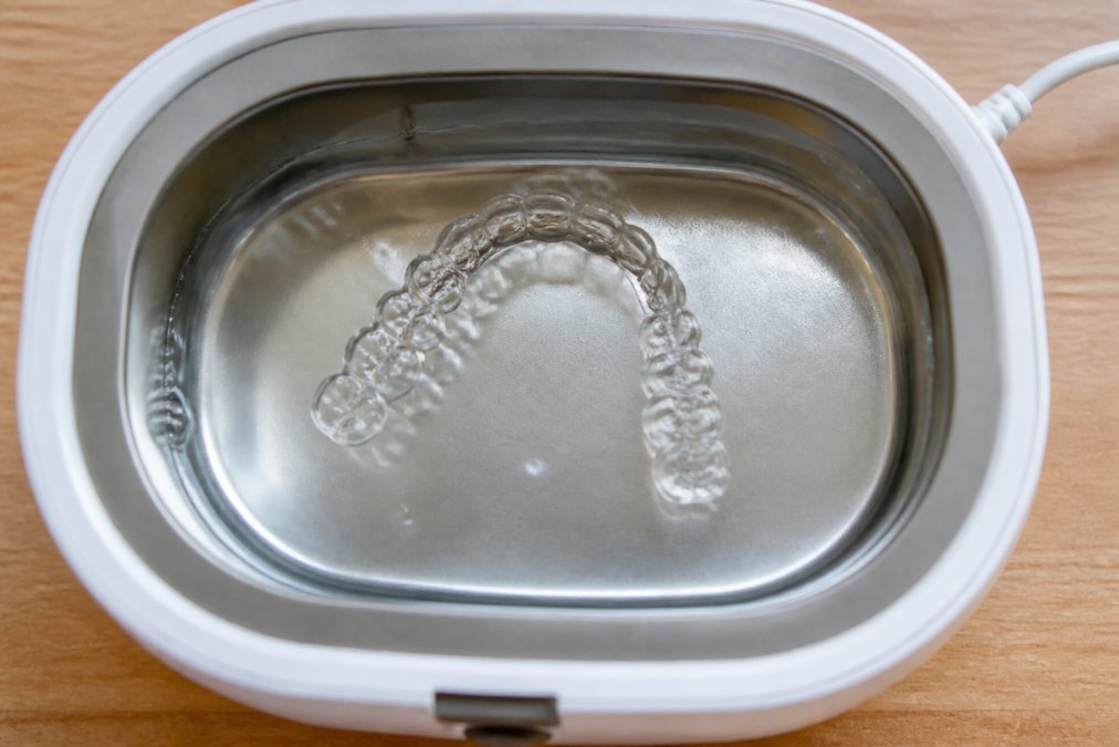 Nahaufnahme eines transparenten Retainers in einer Ultraschallreinigungsschale mit klarer Flüssigkeit, von oben fotografiert mit natürlichem Licht