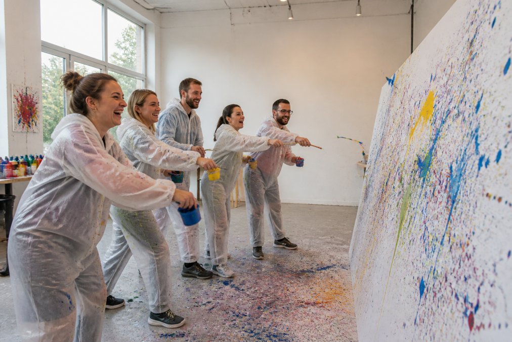 Lachende Erwachsene in Schutzkitteln beim Action Painting im kreativ workshop wien