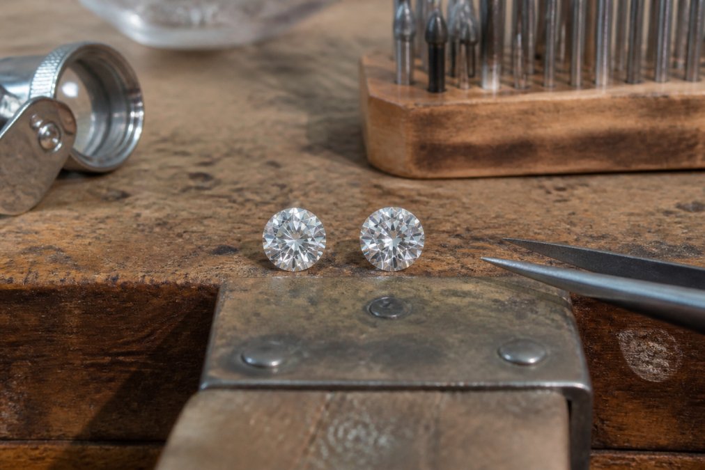 Close-up of a natural diamond and lab-grown diamond side by side on a jeweler's workbench, catching light to show their sparkle and clarity under professional lighting