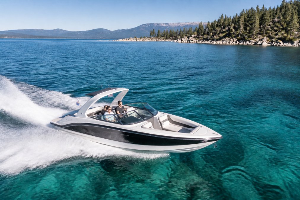 Aerial view of premium Formula 330 SS boat cutting through crystal-clear turquoise Lake Tahoe water on a sunny day, shoreline and pine forests visible in background