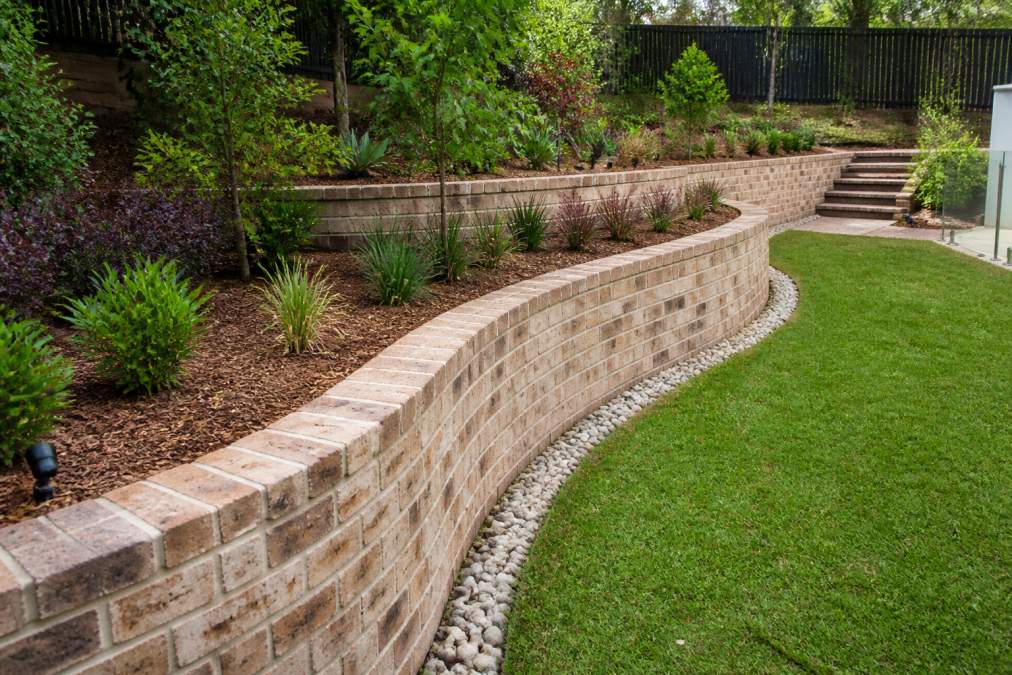 Completed curved retaining wall with integrated garden beds and landscaping, showing quality brick construction, proper drainage, and finished outdoor terraced space