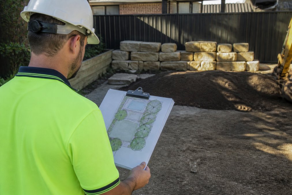 Landscaper Blacktown reviewing a landscape plan in a backyard with sandstone blocks and soil
