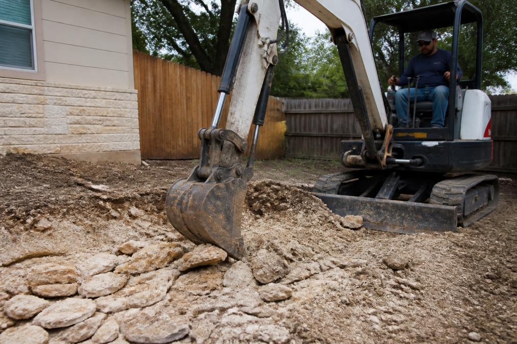 Diagram showing a mini excavator breaking a caliche hardpan layer for successful caliche soil landscaping.