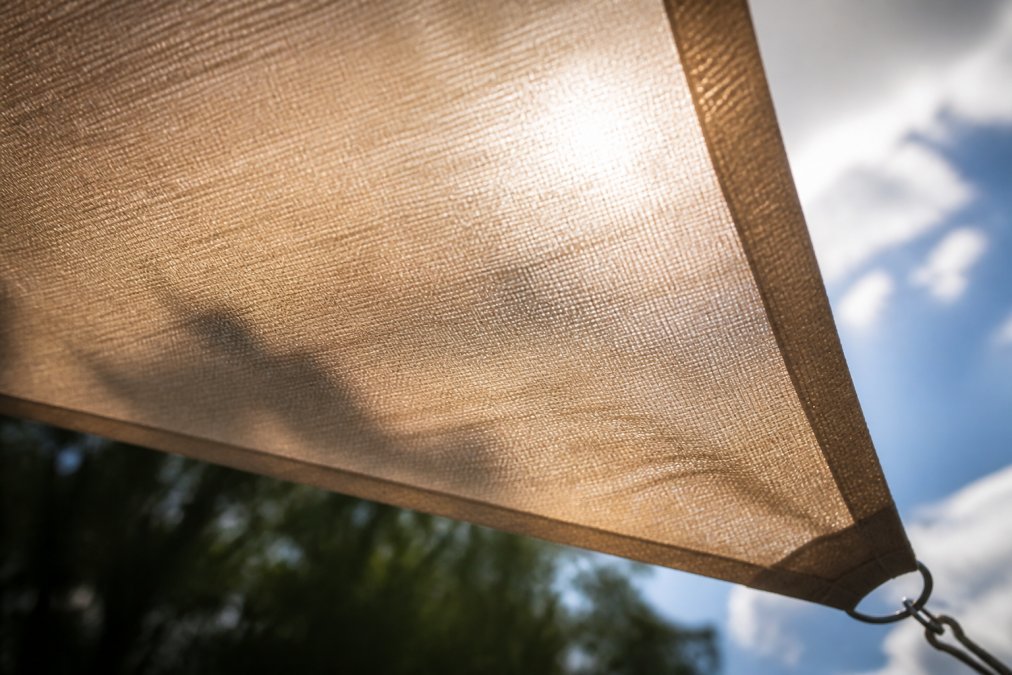 Nahaufnahme von hochwertigem Polyester-Gewebe eines Sonnensegels mit sichtbarer Textur und Verarbeitung, Sonnenlicht durchscheinend