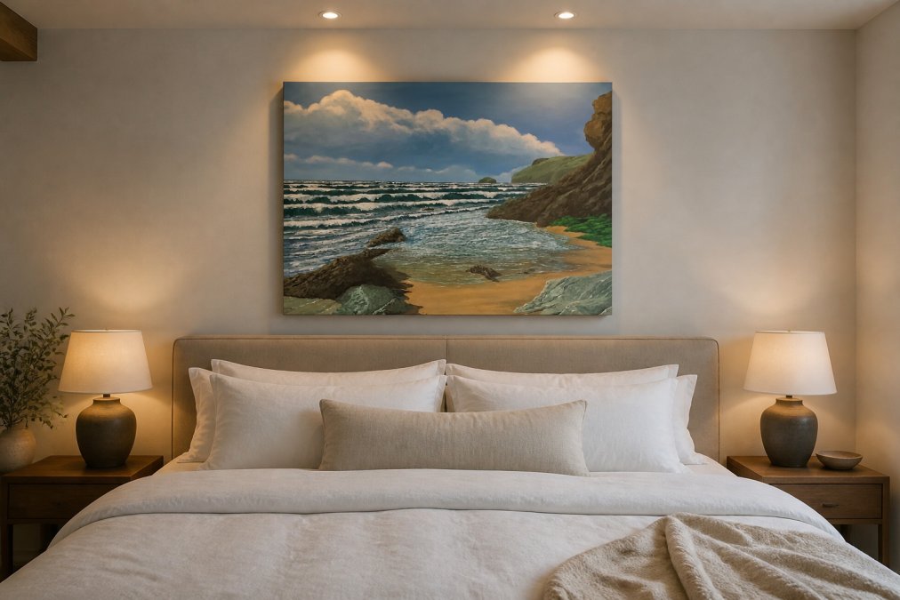 Bedroom with a large coastal landscape canvas print hung above a king-size bed with soft white linens, showing proper sizing and placement with warm accent lighting illuminating the artwork from above