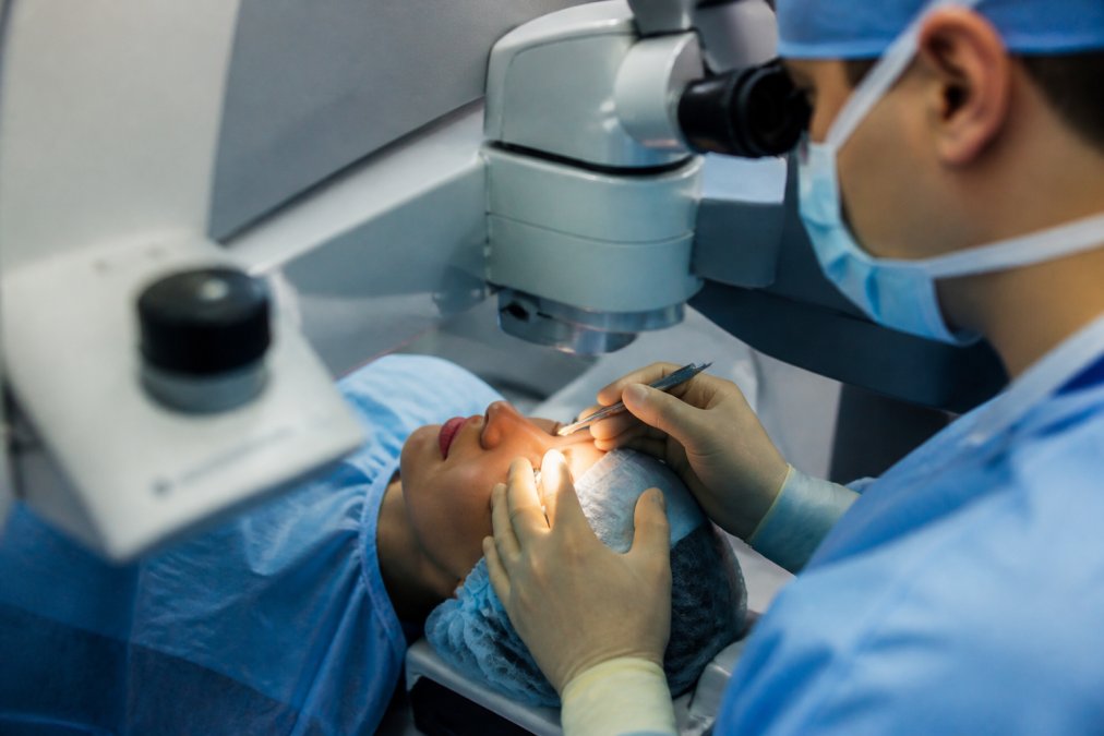 Ophthalmologist performing LASIK surgery with patient positioned under advanced laser equipment in sterile surgical suite, showing precision instruments and patient's eye positioned for treatment