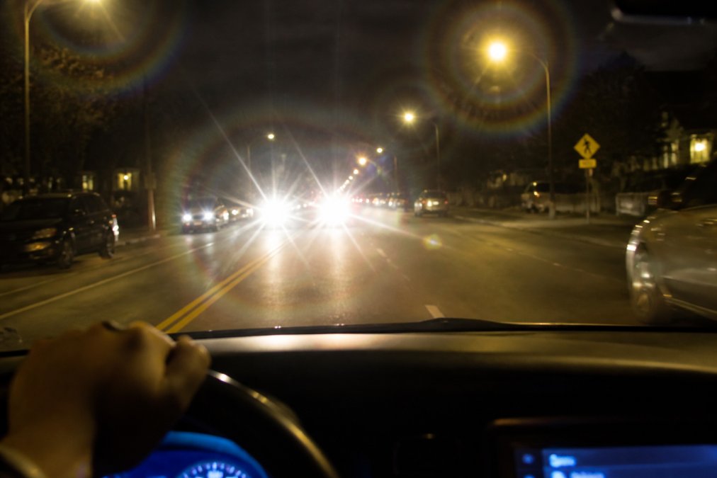 Person driving at night with visible light halos and glare from oncoming headlights and streetlights creating bright rings around light sources in dark driving conditions