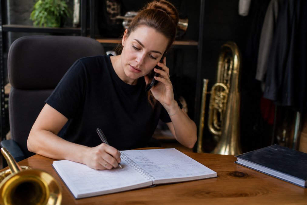 Een evenementenorganisator voert een empathisch telefoongesprek met een klant, met aantekeningen en een kalender zichtbaar op het bureau