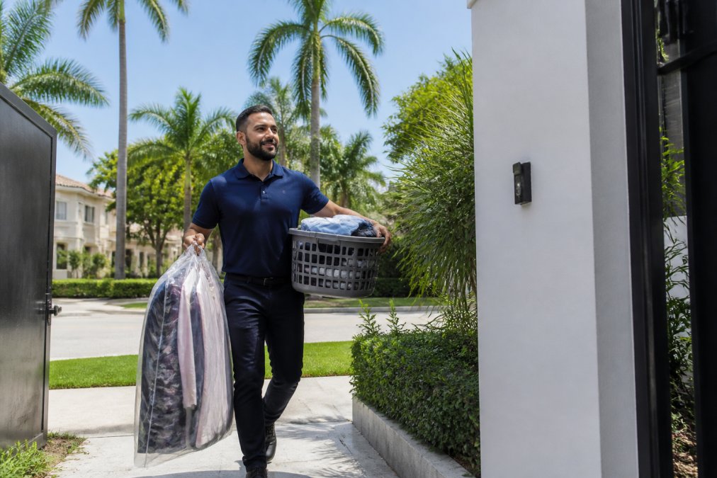 Laundry service professional delivering fresh clothes to a customer's front door in a sunny Miami neighborhood