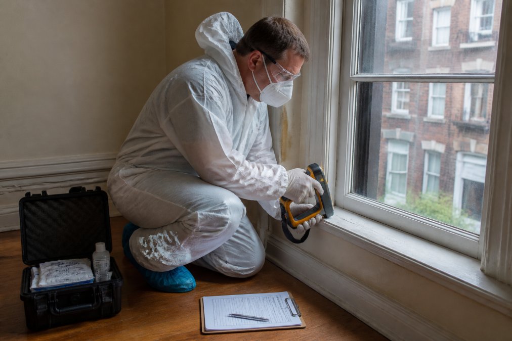 Certified inspector using an XRF analyzer on a windowsill during a lead paint inspection in an apartment.