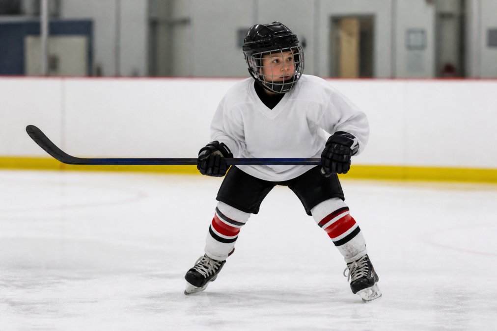 Young hockey player practicing a proper skating stance to learn to play hockey on an indoor rink