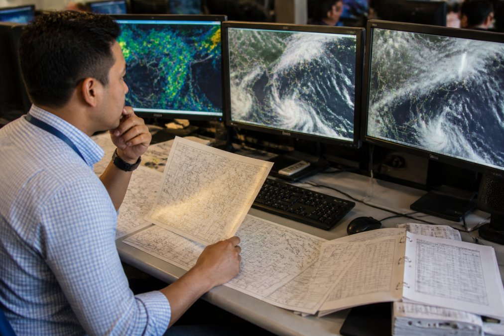 Professional dispatcher studying METAR and TAF reports on multiple computer monitors displaying real-time aviation weather data and forecast charts in an airline operations center