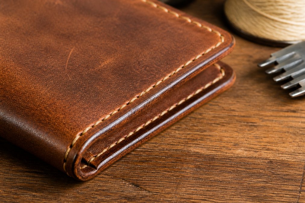 Close-up of hand-stitched leather wallet showing detailed saddle stitch seams and natural patina texture on vegetable-tanned leather