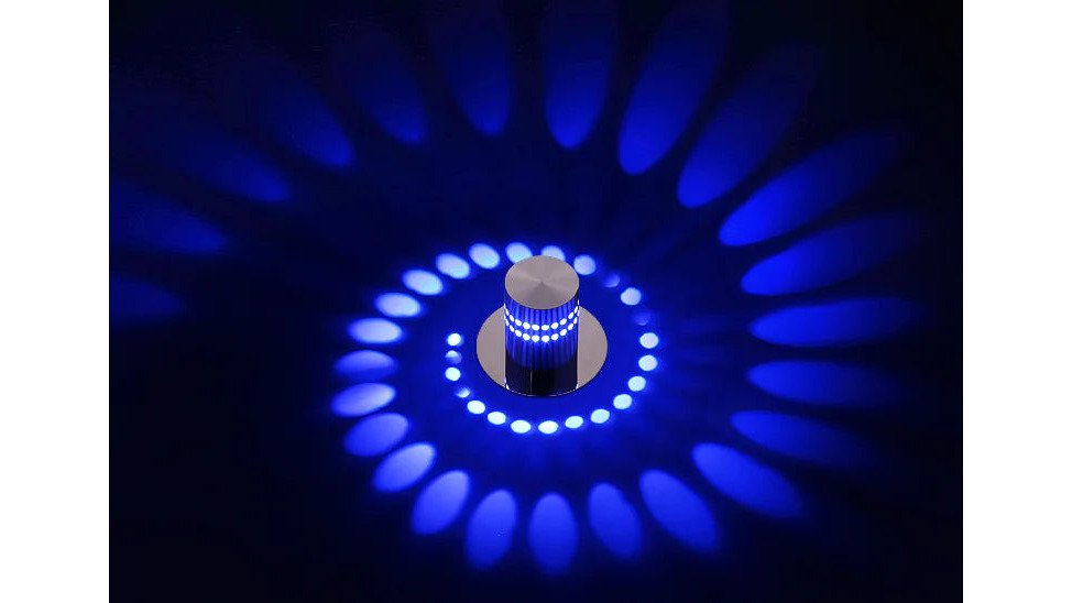 A styled flat-lay on a light wood surface showing a color-changing wall light, a small ceramic incense burner, and a frosted gold ring arranged with eucalyptus sprigs and a linen cloth