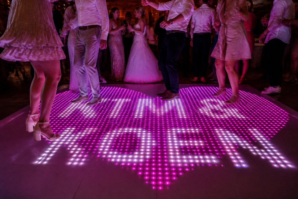 Close-up van LED dansvloer tegels met twinkle effect, sterrenachtig patroon, gasten dansend op de achtergrond, warm licht