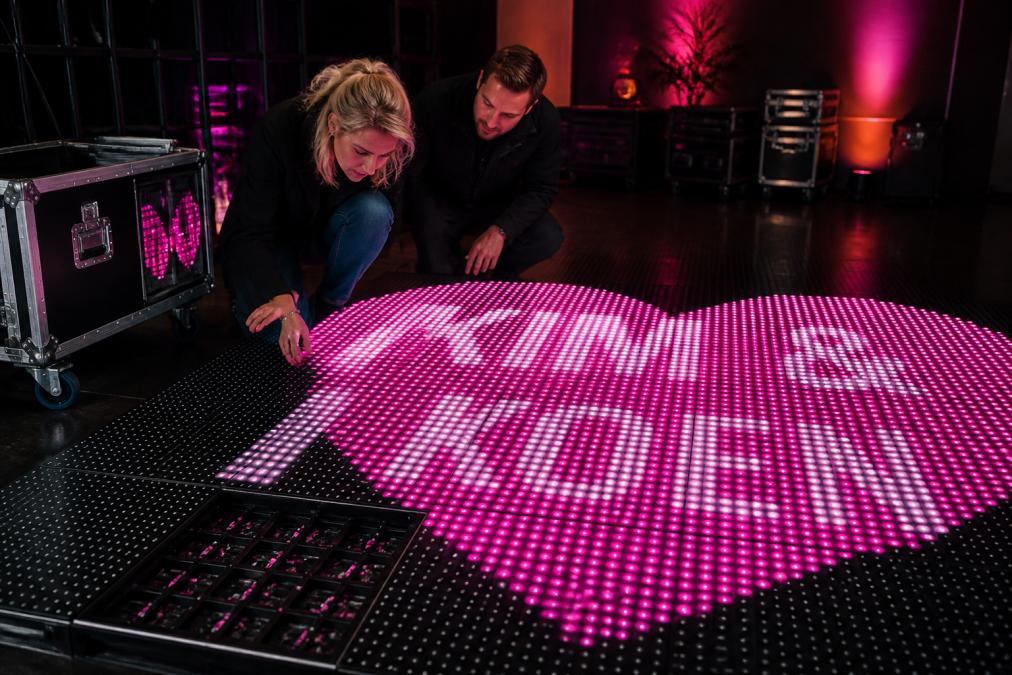 Twee personen onderzoeken de pixelstructuur van een LED dansvloer van dichtbij, waarbij de individuele LED-chips en warmteafvoer duidelijk zichtbaar zijn, in een professionele showroom met goede verlichting