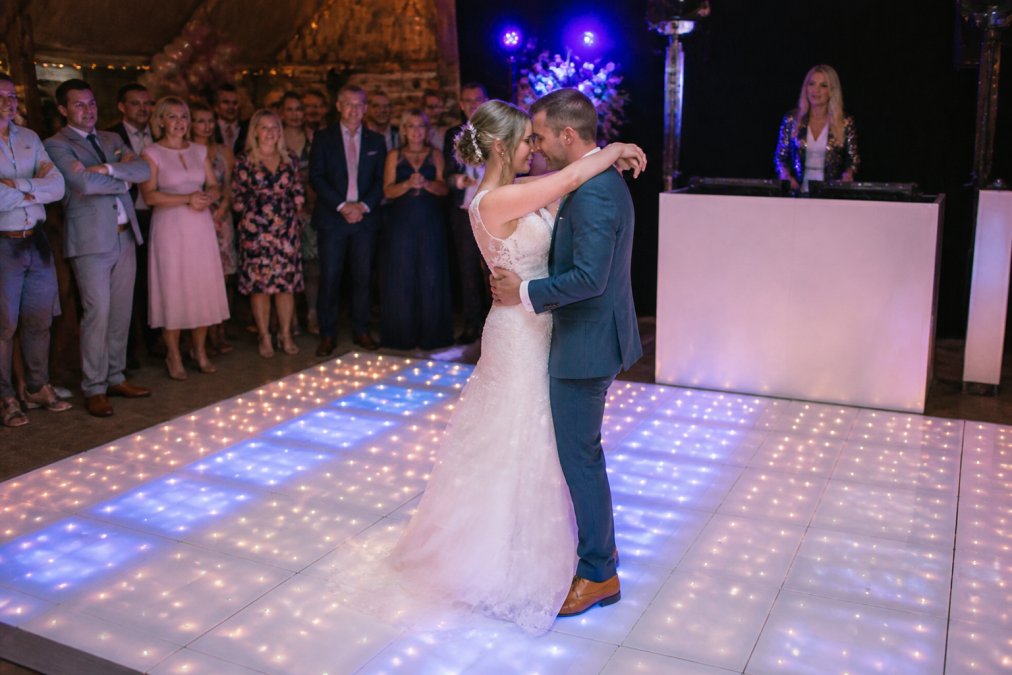 Bruidspaar dansend op een verlichte LED-dansvloer met warm wit en blauw licht, omringd door gasten die toekijken en genieten, foto inclusief Petra Keizer van Gravatar in de achtergrond