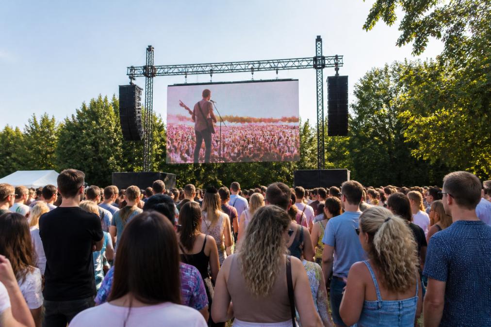 Professioneel LED-scherm van middelgrote formaat geïnstalleerd op een outdoor evenement met bezoekers die naar het scherm kijken, zonlicht dat op het scherm valt, en duidelijk zichtbare beeldkwaliteit ondanks het daglicht