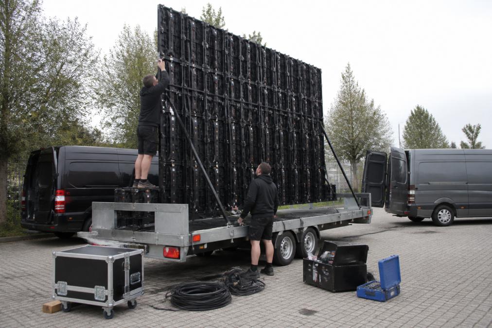 Technische professionals die een LED-scherm op een aanhangwagen installeren, met elektrische kabels, gereedschap en voorbereiding voor transport zichtbaar, constructie in volle gang