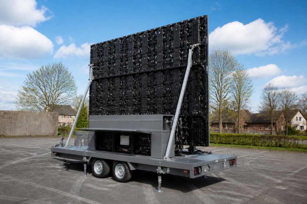 Professioneel LED-scherm gemonteerd op een grijze aanhangwagen, buiten op een parkeerterrein, met duidelijk zicht op de scherminstallatie, het onderstel en de regieruimte aan de achterkant