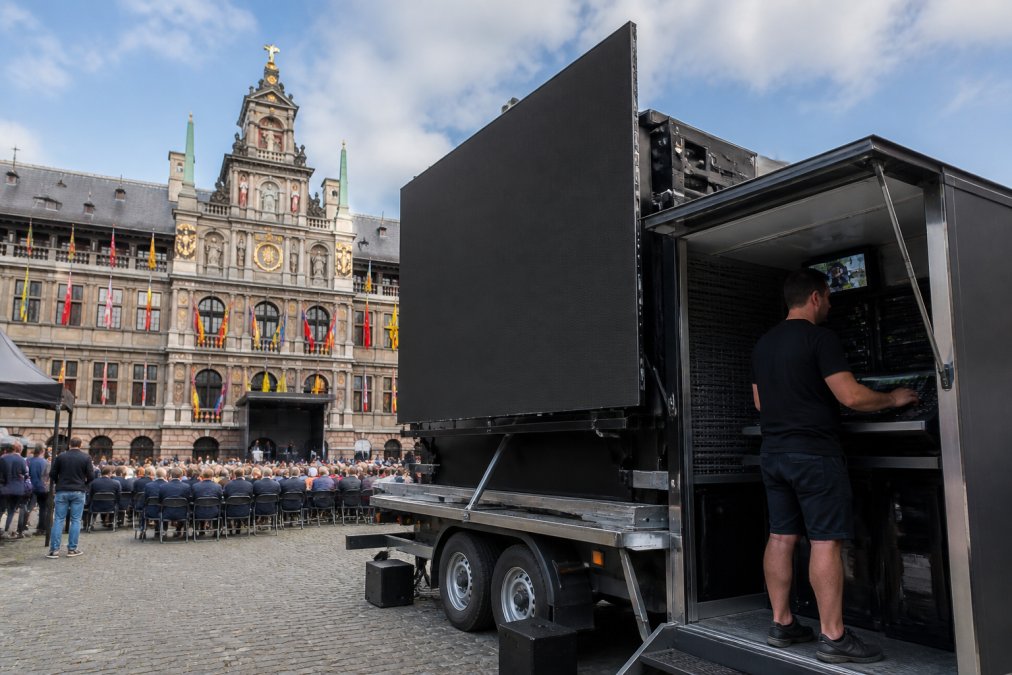 Mobiele LED-scherm aanhanger op locatie tijdens een zakelijk evenement in Antwerpen, met zichtbare regieruimte aan de zijkant en technicus die het scherm bedient via controlekast