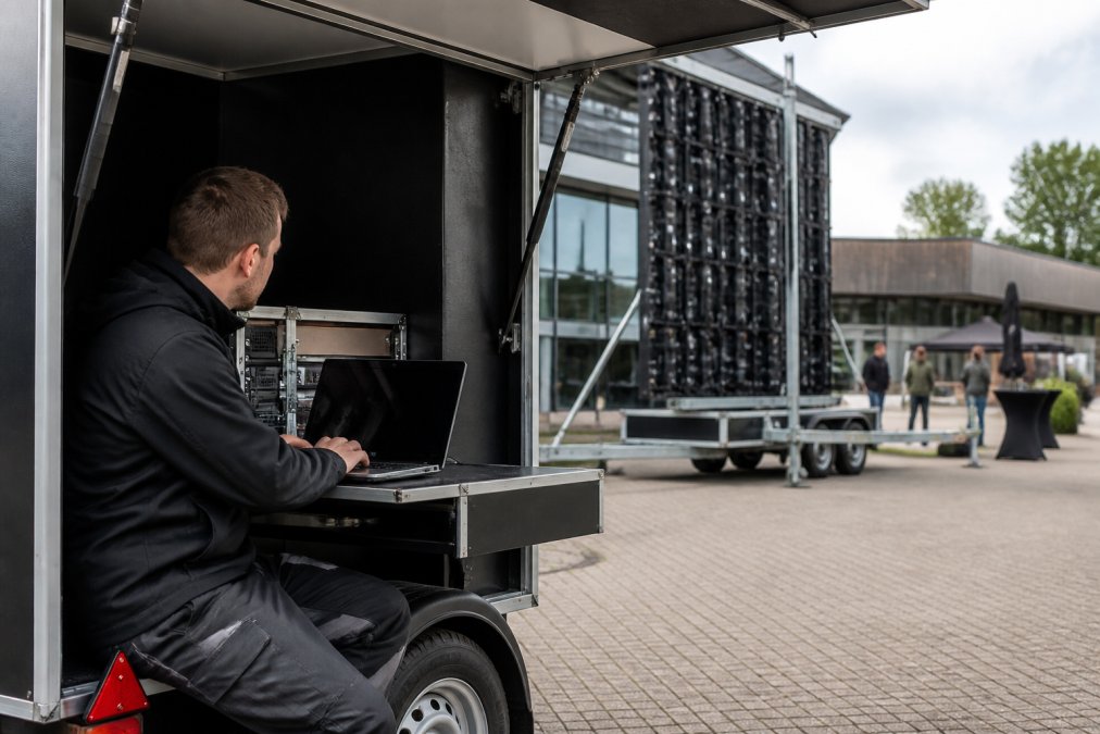 LED trailer met regieruimte opgesteld op een opendeurdaglocatie, met technicus die content op een laptop voorbereidt