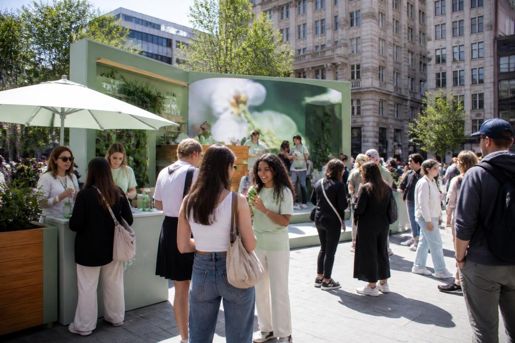 Drukbezochte pop-up store met merkactivatie op een openbaar plein, met consumenten die interactief bezig zijn met producten, natuurlijk daglicht