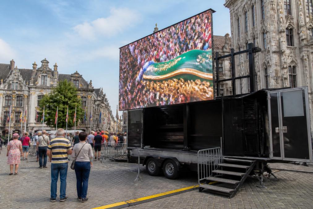 Professionele mobiele LED-scherm aanhangwagen geparkeerd op druk marktplein in Antwerpen, met zichtbare regieruimte aan de zijkant, voorbijgangers kijkend naar het scherm, helder daglicht