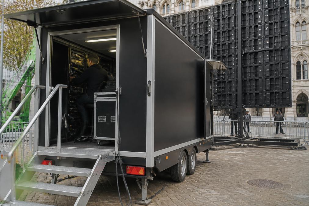 Gesloten aanhangwagen met LED-scherm en regieruimte op een evenementlocatie in Antwerpen, met technicus in de regieruimte bezig met besturing van het scherm