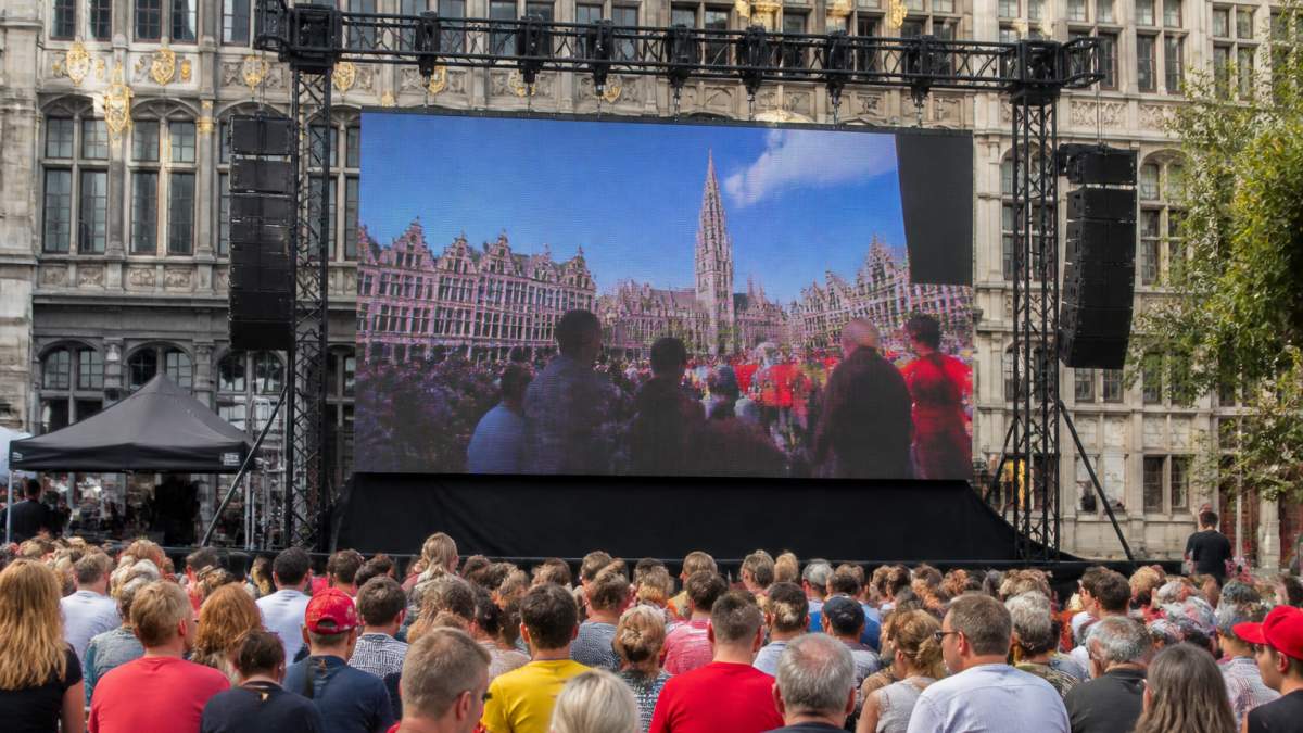 Een groot LED-scherm in werking op een openluchtevenement in Antwerpen met publiek dat de inhoud bekijkt, zonnig daglicht, professionele steunen en kabels zichtbaar