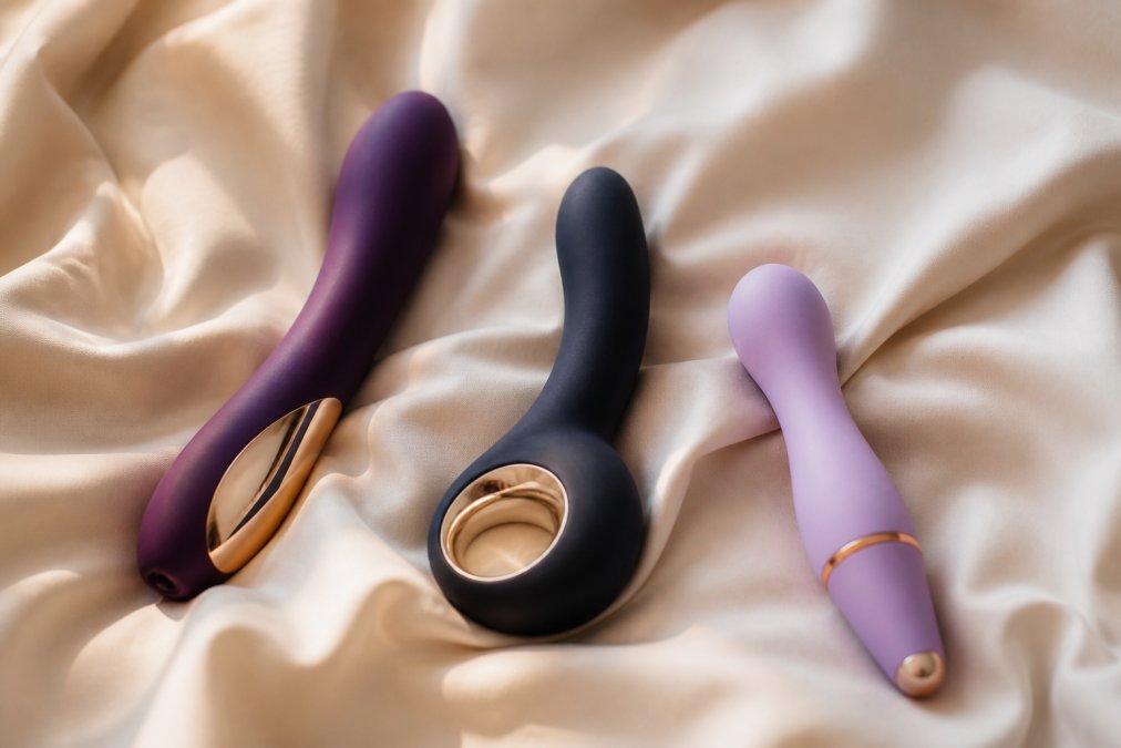 Drie elegante LELO vibrators, de SONA 3, Enigma en Lily 3, liggend op een zachte crèmekleurige zijden stof met zachte natuurlijke lichtinval die de gladde siliconen en het minimalistische design benadrukt