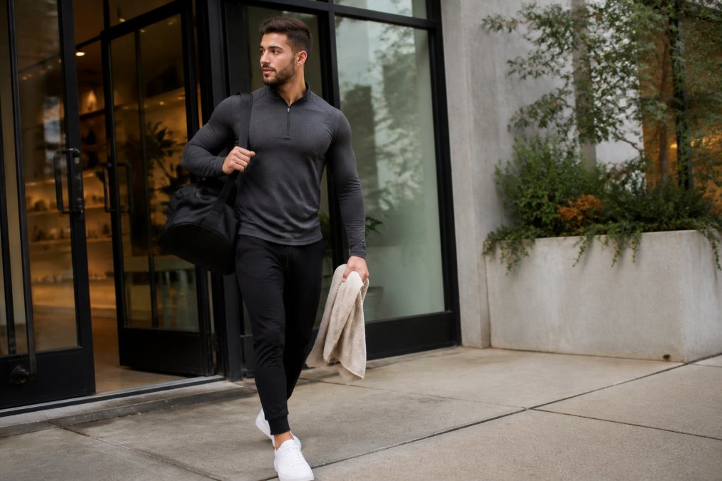 Man transitioning from gym to casual setting, wearing performance activewear that looks polished enough for coffee shop or casual office environment, natural daylight