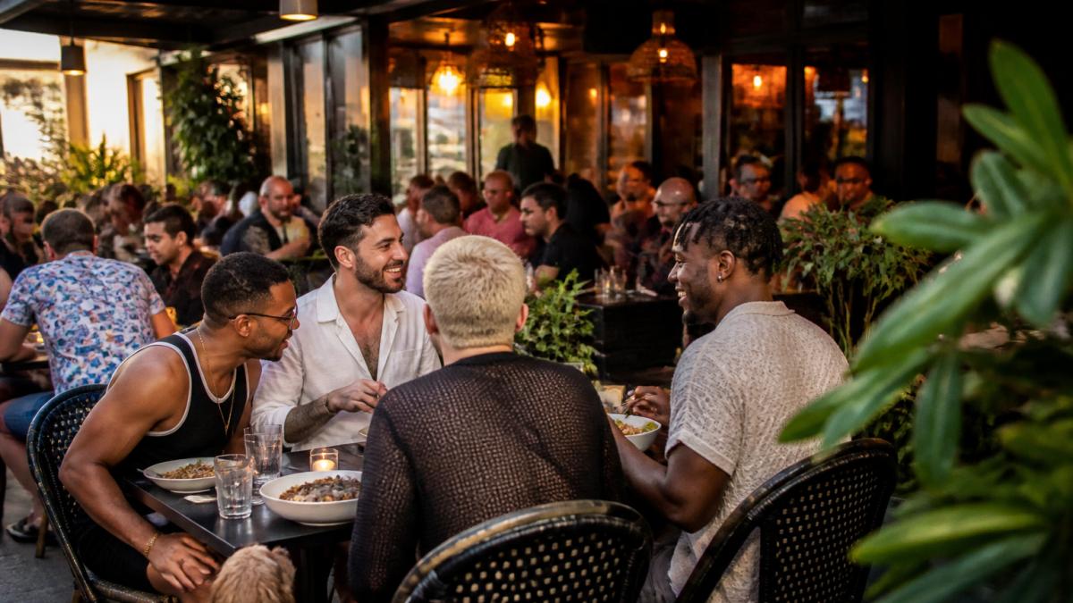 Vibrant dining scene at Robby's West Hollywood with guests laughing and enjoying meals on the pet-friendly patio, warm golden lighting illuminating diverse diners sharing food and conversation, casual elegant decor in background