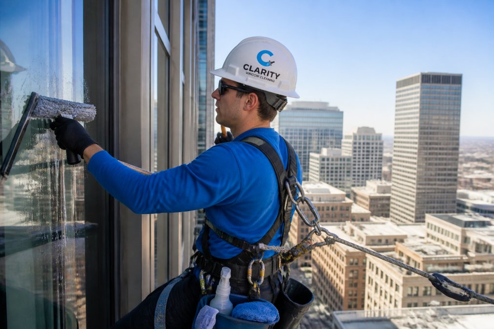 Professional window cleaner in a harness and hard hat, working safely on a high-rise to meet window cleaning insurance