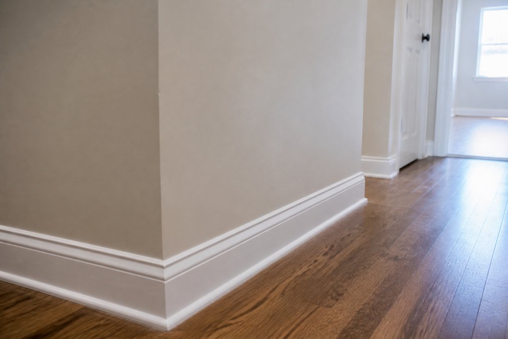 Close-up of a freshly repaired and painted interior wall with crisp new white trim and clean baseboards in a well-lit home hallway, showing precise, professional-quality craftsmanship